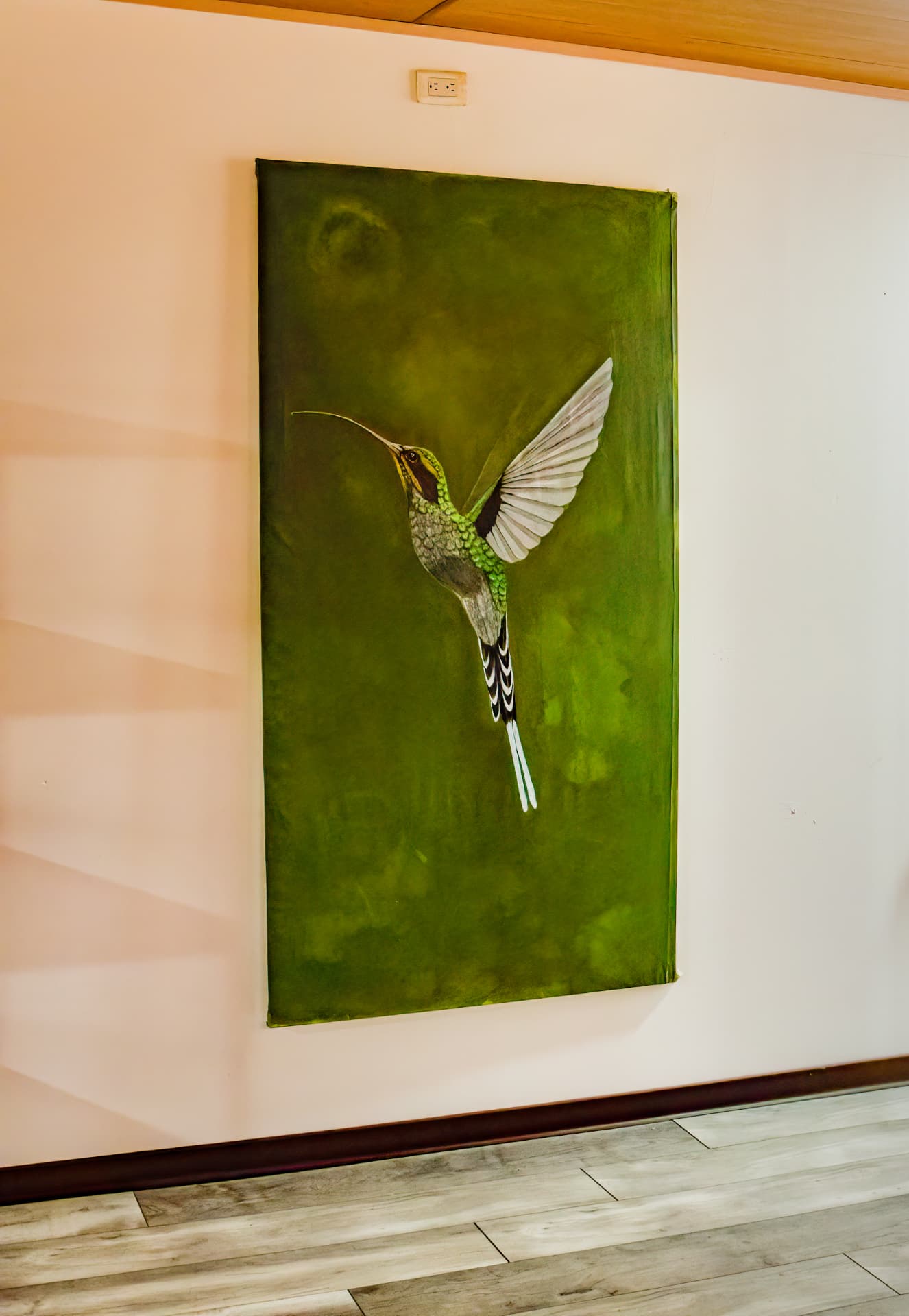 Green hermit hummingbird painting hanging on the white wall of Pizote Apartment