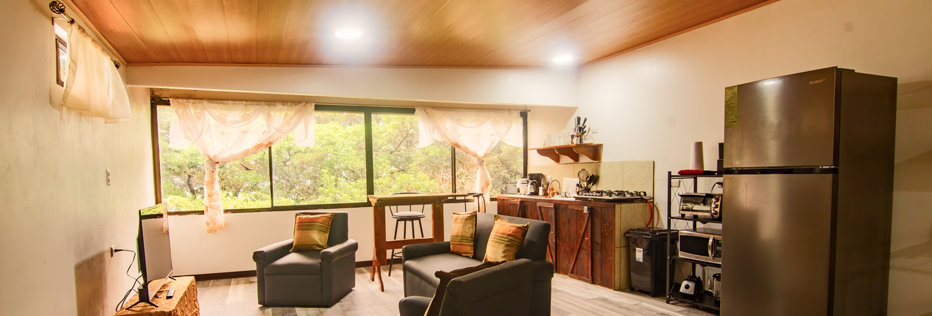Studio living area with sofas, kitchen and a large window onto the trees