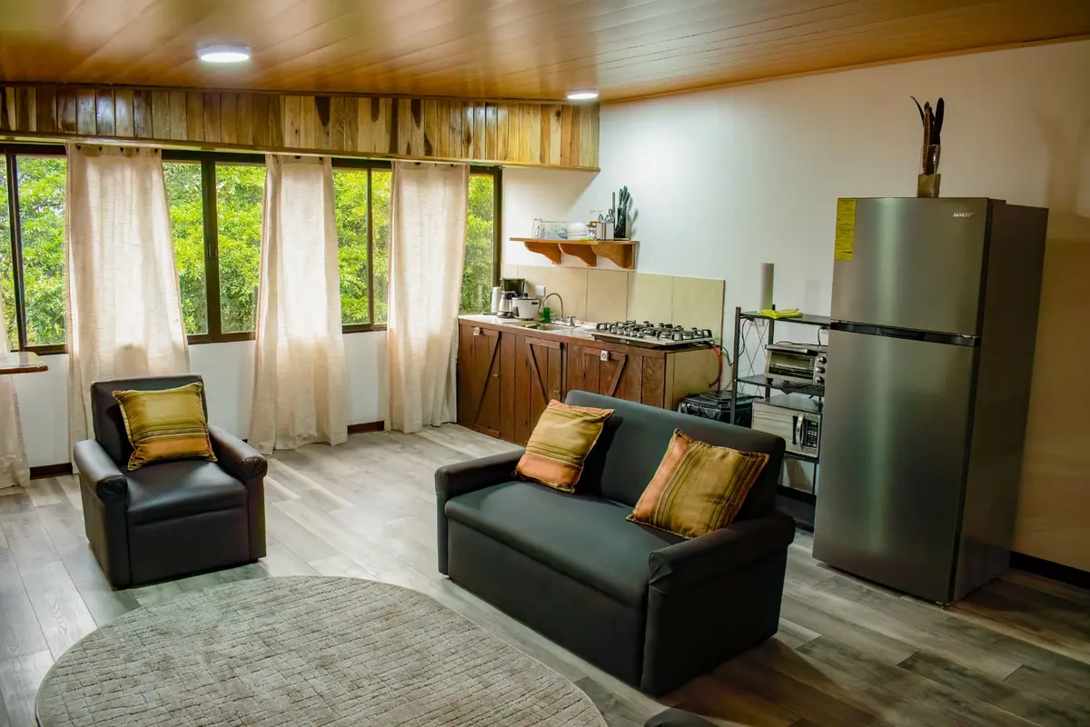 Open-plan living area of Pizote Apartment in Monteverde with sofa, armchair, kitchen and windows onto the trees