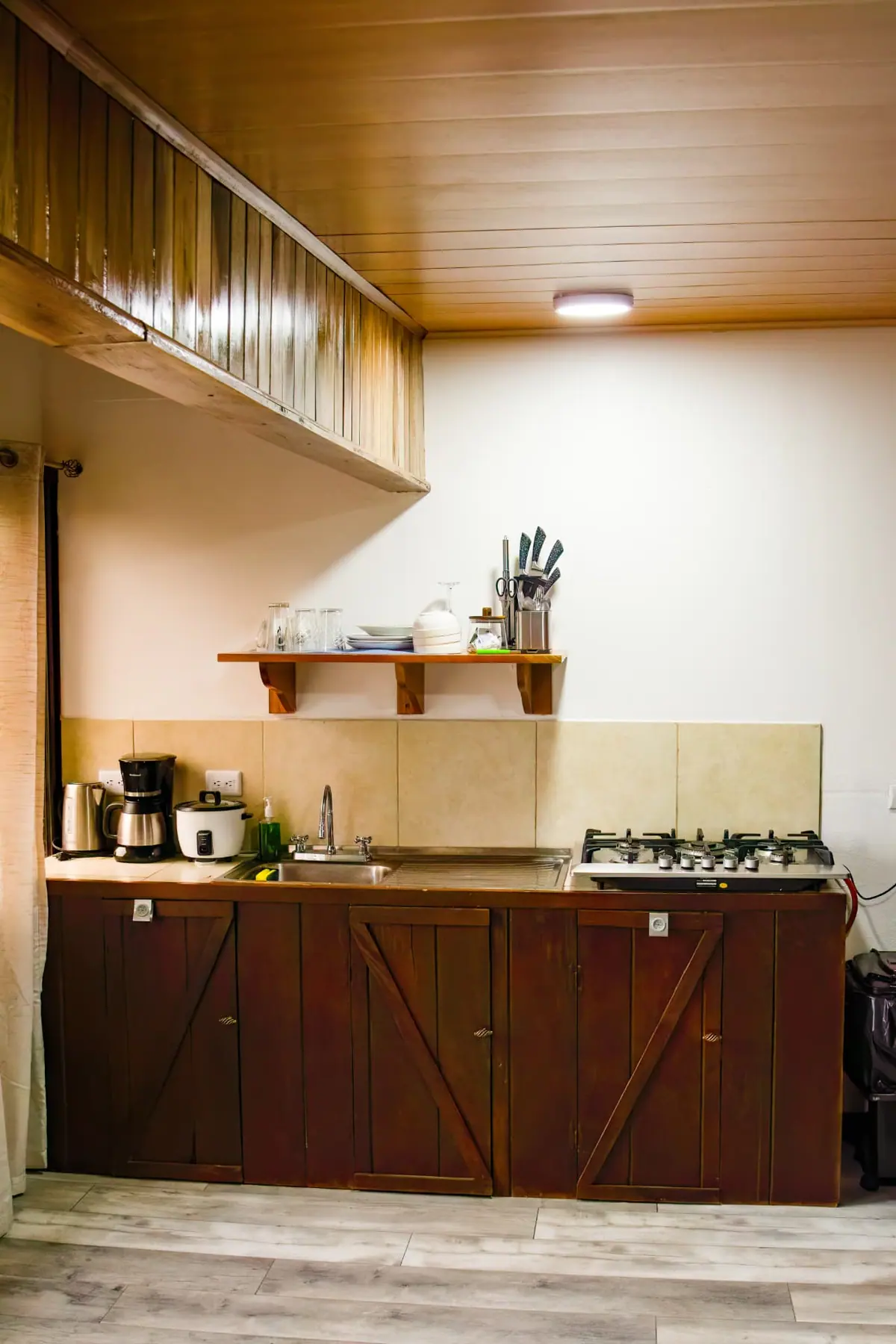 Mesón de cocina con cocina de gas, fregadero, cafetera, hervidor, arrocera y estante con vajilla