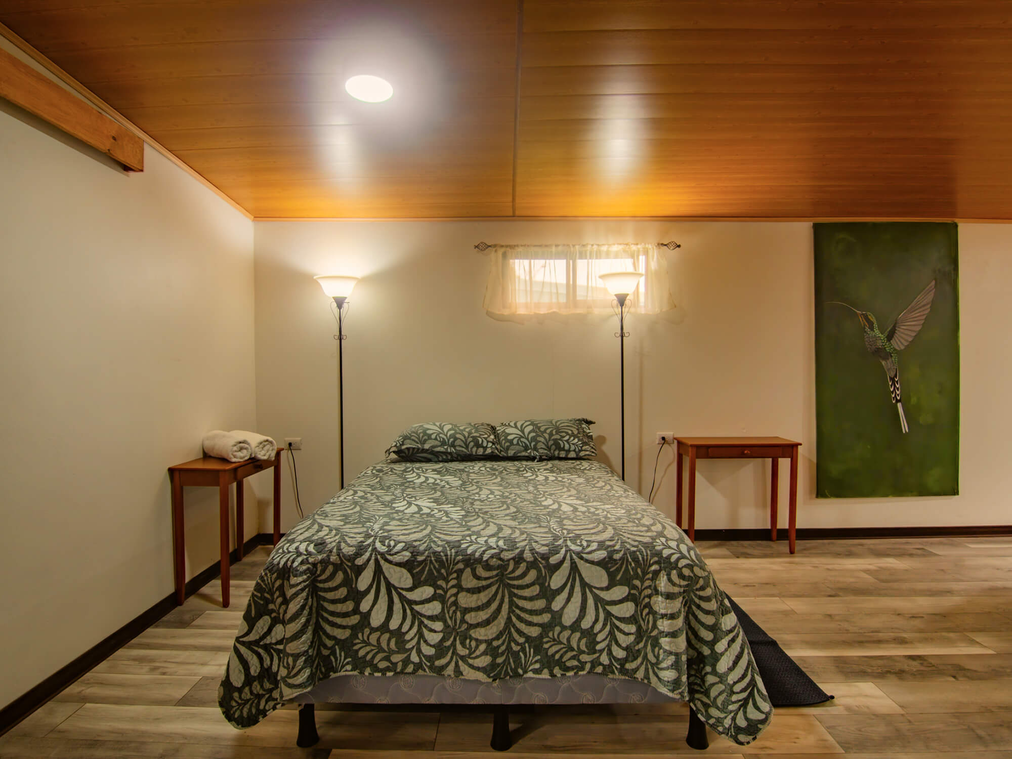 Queen-size bed with leaf-print bedding under the wooden ceiling of Pizote Apartment