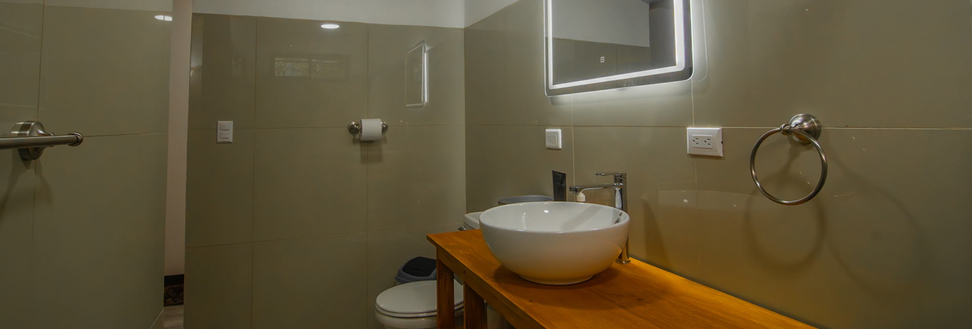 Private bathroom of Pizote Apartment with vessel sink on a wooden counter and glass shower